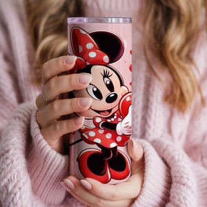 Op de afbeelding: Een roze beker met Minnie Mouse in een rode polkadotjurk en strik. De beker heeft een roze achtergrond met rode hartaccenten. Het ontwerp wikkelt zich om de cilindrische vorm en cre&euml;ert een leuk en kleurrijk drinkgerei.