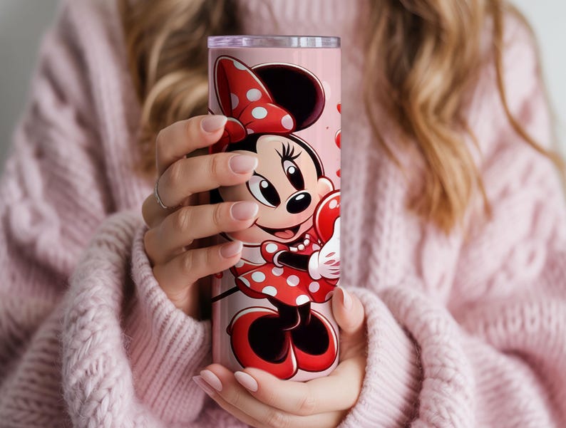 Op de afbeelding: Een roze beker met Minnie Mouse in een rode polkadotjurk en strik. De beker heeft een roze achtergrond met rode hartaccenten. Het ontwerp wikkelt zich om de cilindrische vorm en cre&euml;ert een leuk en kleurrijk drinkgerei.