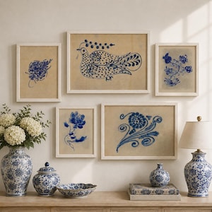May include: A gallery wall arrangement featuring five framed prints with blue ink illustrations of birds and floral motifs on a tan background. Below, blue and white ceramic vases, a lidded jar, a bowl, and a table lamp with a white shade.