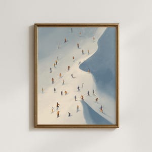 May include: Art print in a gold frame showing a snowy mountain with skiers and snowboarders. The artwork has a minimalist style, with white, blue, and orange tones. The skiers are spread across the slope, creating a sense of movement and activity.