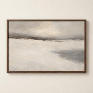 Op de afbeelding: Een rechthoekig landschapsschilderij in een donkerbruine houten lijst, met een besneeuwd veld onder een bewolkte, grijze lucht. De scène bevat gedempte tinten wit, grijs en zachtbruin, met een donkergrijze waterpartij op de voorgrond.