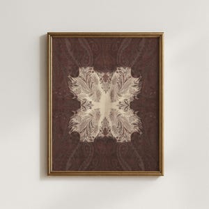 May include: Framed artwork featuring a symmetrical paisley pattern in shades of brown and cream. The artwork has a gold-colored frame. The central design is a cream-colored, ornate floral motif, surrounded by a darker brown paisley background.
