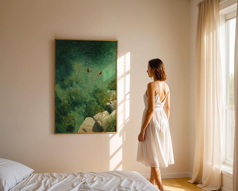 May include: A framed painting with a gold border depicts two figures swimming in turquoise water. A woman in a white dress stands in front of the artwork, near a bed with white linens. Sunlight streams through a window.