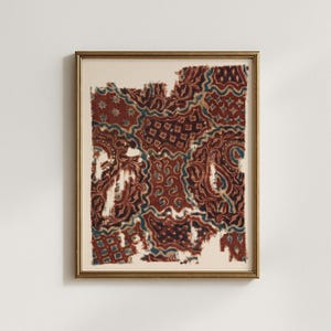 May include: Framed artwork featuring a fragment of patterned fabric. The fabric displays a complex design in shades of burgundy, teal, and cream, with intricate floral and geometric motifs. The artwork is encased in a gold-toned frame, adding a touch of elegance.