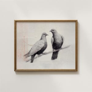 May include: A framed artwork featuring two doves perched on a branch. The birds are rendered in grayscale, with detailed shading and texture. The artwork is set against a textured white background, framed in a gold-colored frame.
