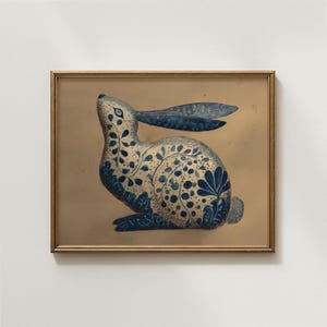 Könnte beinhalten: Gerahmter Druck mit einer blau-weißen Hasenillustration. Der Hase ist mit floralen und Punktmustern verziert. Das Kunstwerk ist vor einem beigefarbenen Hintergrund platziert und in einem goldfarbenen Rahmen eingefasst. Der Hase blickt nach oben.