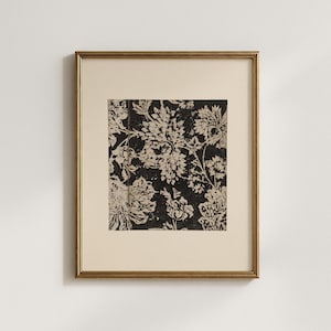 May include: A framed print featuring a black and cream floral pattern. The artwork is displayed within a gold-colored frame, set against a cream-colored mat. The floral design is detailed, with a vintage aesthetic. The print is a square shape.