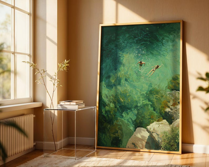 May include: A framed art print depicts two figures swimming in turquoise water. The artwork, with a gold frame, is displayed against a beige wall. The scene captures a serene moment with sunlight streaming through a nearby window.