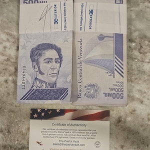 May include: Stacks of Venezuelan 500 Mil Bolivares banknotes, featuring a portrait and a flag design. A certificate of authenticity from The Patriot Vault is also present, with text about the currency's legitimacy.
