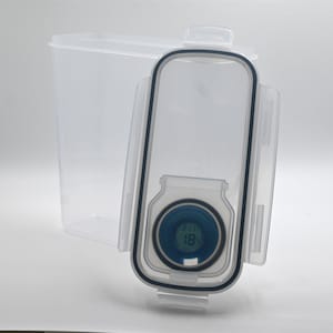 May include: A clear, rectangular food storage container with a digital display on the lid. The display shows the temperature in blue digits. The lid has a black seal and a clear plastic latch.