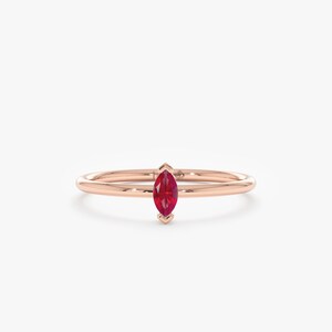 May include: A rose gold ring featuring a marquise-cut, vibrant red gemstone. The gemstone is set in a delicate, minimalist design, showcasing the stone's shape and color. The ring's band is thin and polished.