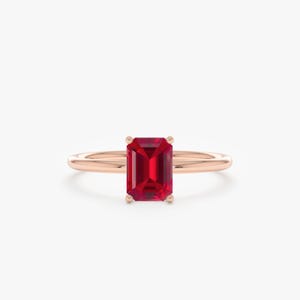 Peut inclure: Une bague en or rose ornée d'une pierre précieuse rouge foncé de forme rectangulaire. La pierre précieuse est le point central, sertie dans un anneau simple et élégant. Le design de la bague est minimaliste.