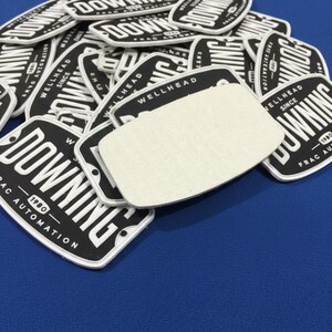 May include: A pile of black and white rectangular patches with the word "DOWNING" in bold white letters. The patches also include the text "FRAC AUTOMATION" and "WELLHEAD SINCE 1980". A blank white patch is on top.