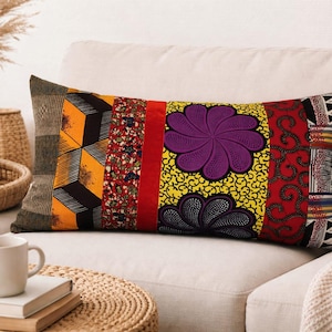 Może przedstawiać: Prostokątna poduszka dekoracyjna z żywym wzorem patchworkowym. Poduszka posiada geometryczne wzory, motywy kwiatowe i duży fioletowy kwiat na żółtym tle. Paleta kolorów obejmuje pomarańczowy, czerwony, czarny i żółty.