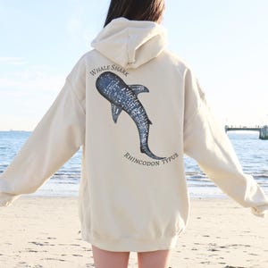 Könnte beinhalten: Cremefarbener Kapuzenpullover mit einem Walhai-Motiv auf dem Rücken. Das Design zeigt eine detaillierte Illustration des Walhais mit den Worten "WHALE SHARK" und "RHINCODON TYPUS" in kreisförmiger Anordnung.