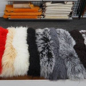 May include: A variety of fluffy sheepskin rugs in different colors, including turquoise, cream, purple, red, white, black, gray, and brown. The rugs are arranged in a row on a wooden surface.