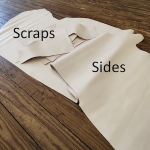 Puede incluir: Primer plano de dos piezas de cuero de color blanco roto. Una pieza está etiquetada como "Scraps" y la otra como "Sides".