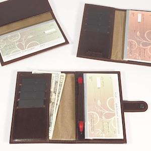 Könnte beinhalten: Ein braunes Leder-Scheckbuch-Etui mit Stifthalter und Steckplätzen für Kreditkarten. Das Etui ist geöffnet und zeigt einen Scheck und Bargeld im Inneren.