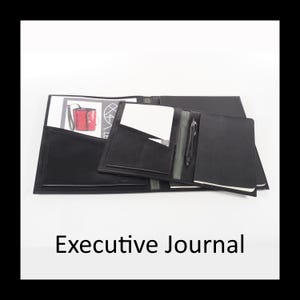 Op de afbeelding: Een zwarte executive journal map met een lederlook, voorzien van meerdere binnenvakken, een penhouder met een zwarte pen en een notitieblok. De linkerkant bevat een documentenvak met een papieren inlegvel, de rechterkant een notitieboek.