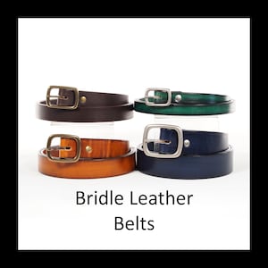 Op de afbeelding: Vier leren riemen in bruin, groen, oranje en marineblauw, elk met een metalen gesp. De riemen worden gepresenteerd tegen een witte achtergrond. De tekst "Bridle Leather Belts" staat onderaan de afbeelding.