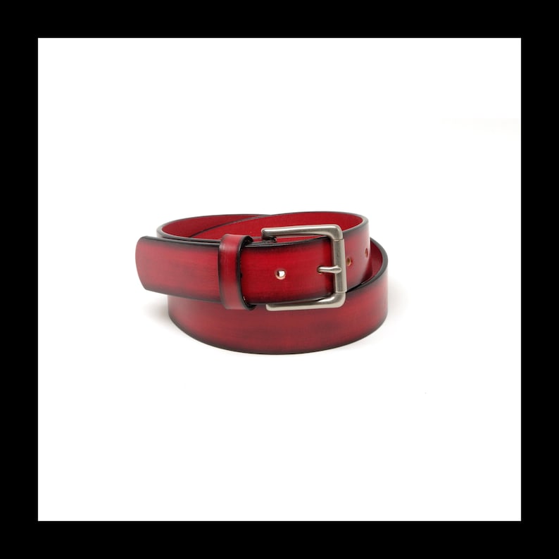 May include: A red leather belt with a silver-colored buckle. The belt is a deep shade of red with a slightly distressed finish. The buckle is rectangular and has a classic design.