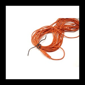 May include: A coiled orange electrical cable against a white backdrop. The cable has a connector at one end and is secured with a black tie. The cable is a bright orange colour.