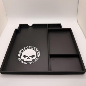 Könnte beinhalten: Schwarze Organizer-Ablage mit mehreren Fächern und einem Ausschnitt. Das Tablett zeigt ein weißes Harley-Davidson-Schädellogo. Das Tablett dient zur Aufbewahrung verschiedener Gegenstände und zur Organisation.