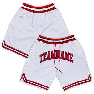 May include: White basketball shorts with red and black trim. The shorts have a red drawstring and the text "TEAMNAME" in red block letters. The shorts have two pockets on the back.
