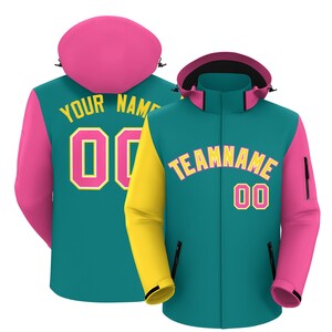 May include: A teal hooded jacket with a pink hood and sleeves, featuring a yellow sleeve on the right. The front displays the text TEAMNAME and the number 00 in yellow and pink. The back shows YOUR NAME and the number 00 in yellow.