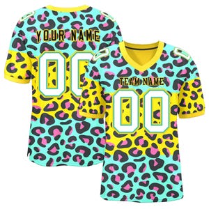 Könnte beinhalten: Zwei Football-Trikots mit einem lebendigen Leopardenmuster in Gelb, Türkis und Pink. Die Trikots haben einen gelben Kragen und Ärmel, mit der Nummer "00" in Weiß. Ein Trikot trägt die Aufschrift "YOUR NAME" und das andere "TEAM NAME".