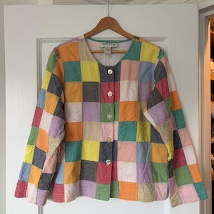 May include: A long-sleeved jacket featuring a multi-colored patchwork design with squares in shades of yellow, orange, pink, green, blue, and grey. The jacket has a round neckline, a front button closure with five light-colored buttons, and an Orvis label.