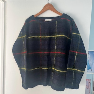 May include: A navy blue sweater with a plaid pattern in red and yellow lines. The sweater is hanging on a wooden hanger. The label reads "CAROLYN TAYLOR NEW YORK".