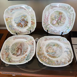 Peut inclure: Quatre assiettes carrées en céramique ornées d'illustrations de Beatrix Potter. Les assiettes représentent Mrs. Tiggy-Winkle, Jemima Puddle-Duck, Benjamin Bunny et Mr. Jeremy Fisher, avec leurs noms et la signature Beatrix Potter imprimés.