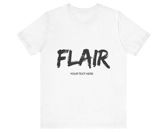May include: A white short-sleeved t-shirt featuring the word FLAIR printed in a large, black, brush-stroke style font across the chest, with the smaller text YOUR TEXT HERE printed in a simple black sans-serif font directly underneath it.