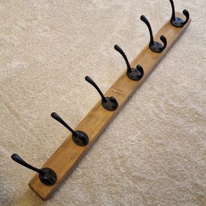 May include: A wooden coat rack with six black metal hooks. The rack is made of light brown wood and the hooks are evenly spaced along the length of the board. The hooks have a curved design.