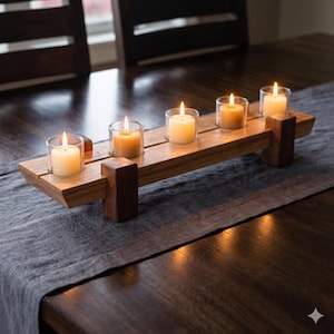 May include: A rectangular wooden candle holder featuring five clear glass votive cups, each containing a lit white candle. The holder is constructed from light-toned wood with dark wood support blocks at each end, creating a linear centrepiece.