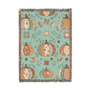 May include: A woven throw blanket featuring a light teal background with a repeating pattern of pumpkins, stars, and autumn leaves. The pumpkins are decorated with various floral, plaid, and checkered prints in shades of orange, green, and cream.