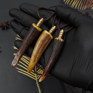 May include: Three antler pendant necklaces with brass accents and brown cords. The pendants are various shades of brown and yellow. The necklaces are displayed against a black background.