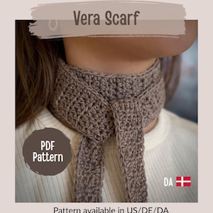 May include: A crocheted scarf in a neutral brown color, tied around the neck. The scarf is labeled "Vera Scarf" and the image includes the text "PDF Pattern". The pattern is available in US/DE/DA.