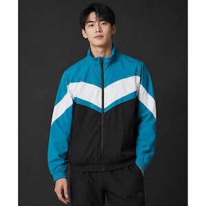 Puede incluir: Chaqueta deportiva turquesa, blanca y negra con cierre de cremallera completo. La chaqueta presenta un diseño de bloques de color con rayas blancas en forma de chevrón en el pecho y los hombros. Cuello alzado y puños elásticos.