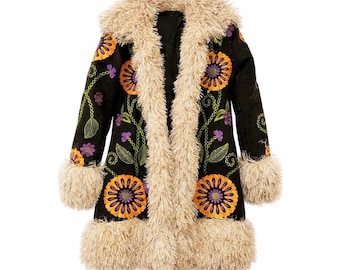 Peut inclure: Un manteau noir avec un col, des poignets et une bordure en fausse fourrure crème. Le manteau présente des motifs floraux orange et violets brodés avec des vignes et des feuilles vertes. Le manteau est de style long et bohème.