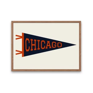 Può includere: Una stampa incorniciata in stile gagliardetto con la scritta "CHICAGO" in lettere arancioni su sfondo blu navy. La stampa è posta su uno sfondo bianco sporco e incorniciata in una cornice di legno marrone chiaro.