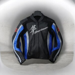 May include: Black leather motorcycle jacket with blue and silver detailing. The jacket displays the word "Hayabusa" in white script on the chest. Red accents are visible on the shoulders. It has a zip-up front and two pockets.