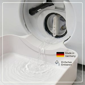 Puede incluir: Primer plano de un componente blanco de lavadora con agua fluyendo hacia un recipiente blanco. La imagen incluye el texto "Made in Germany" y "Einfaches Entleeren".
