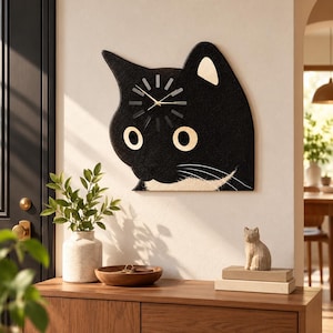 May include: A black cat-shaped wall clock with large, round, light-colored eyes and a white chin detail. The clock face features thin, dark hands and simple hour markers, mounted on a wall above a wooden cabinet with a plant and decor.