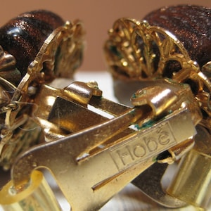 Puede incluir: Pendientes de clip de tono dorado con detalles de filigrana marrón y dorado. Los pendientes están marcados con "Hobe".