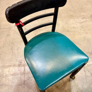 May include: A vintage chair with a black wooden frame and a teal seat. The backrest is curved and the seat is padded. The chair has four legs with decorative brass feet. The chair is likely from the mid-20th century.