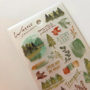 May include: A sheet of watercolor-style stickers with nature-themed designs. The stickers feature trees, birds, leaves, and phrases like "A Tiny Leaf" and "Strike Into The Woods." The color palette includes greens, browns, and oranges.