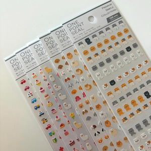 Peut inclure: Plusieurs feuilles d'autocollants avec de petits autocollants 3D colorés. Les autocollants représentent diverses races de chiens, des cupcakes, des voitures et d'autres motifs mignons. L'emballage comprend le texte "ONE POINT SEAL" et "PREMIUM SIMPLE COLLECTION".