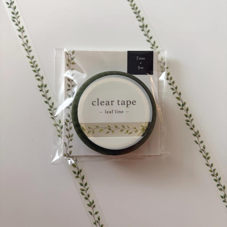 May include: A roll of clear tape with a green leaf design, packaged in a clear plastic sleeve. The tape roll is labeled "clear tape - leaf line -" and measures 7mm x 5m.